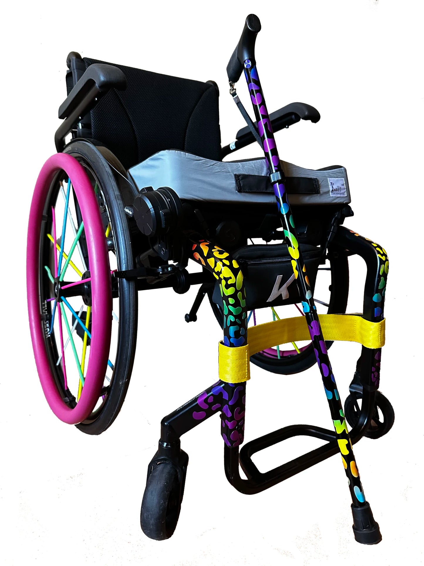 Musta pyötäruoli, jonka renkaissa pinkit kelausvanteen suojat ja moniväriset pinnakuoret. Runossa Wheelchair Skins retroheijastavat tarrat leopardikuosissa, monivärinen